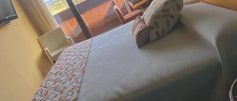 A hotel room with a large bed, a desk, a chair, a TV, and a view of the outdoors.