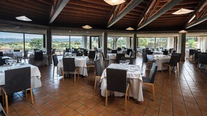 A spacious restaurant with multiple tables and chairs, large windows offering a view of the outdoors, and a wooden ceiling structure. - Hotel 4* Parque de Monfragüe (Torrejon El Rubio)