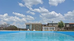 A swimming pool with clear blue water, surrounded by modern buildings with large windows and a stone facade. - Hotel 4* Parque de Monfragüe (Torrejon El Rubio)