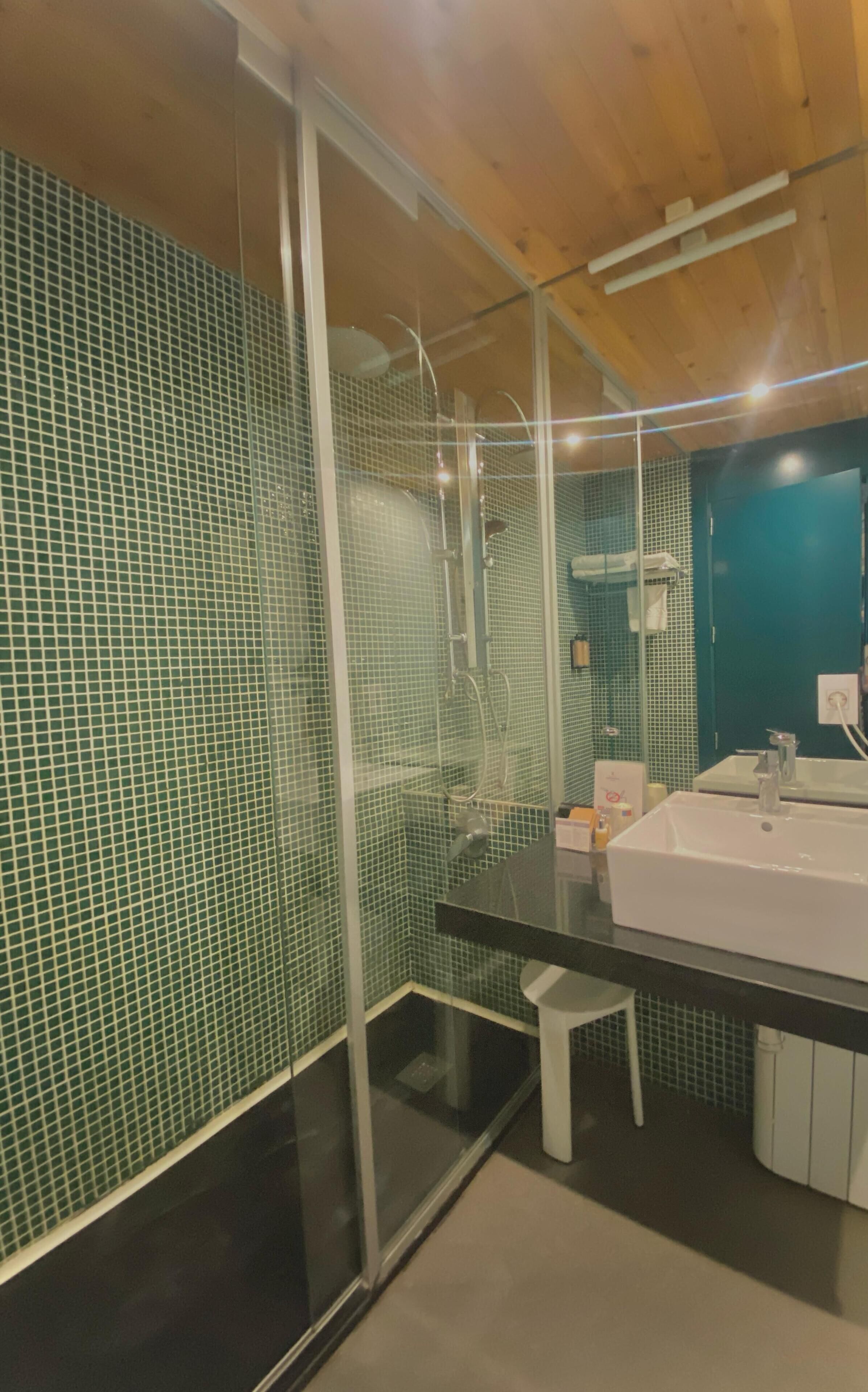Un baño moderno con cabina de ducha de vidrio, un lavabo blanco y paredes con azulejos verdes.