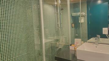 Un baño moderno con cabina de ducha de vidrio, un lavabo blanco y paredes con azulejos verdes.