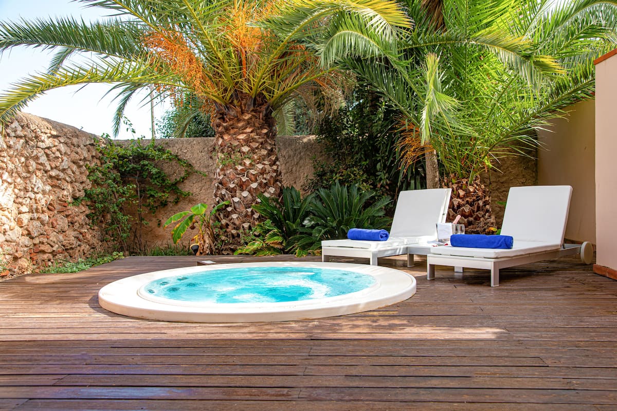 Un jacuzzi rodeado de sillones de descanso y palmeras en una terraza de madera.