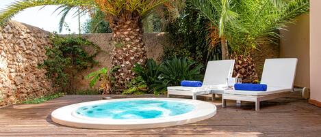Un jacuzzi rodeado de sillones de descanso y palmeras en una terraza de madera.