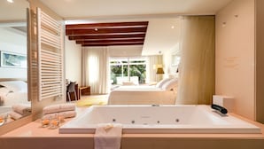 A modern hotel room with a large bathtub, a mirror, and a view of the garden through the window.
