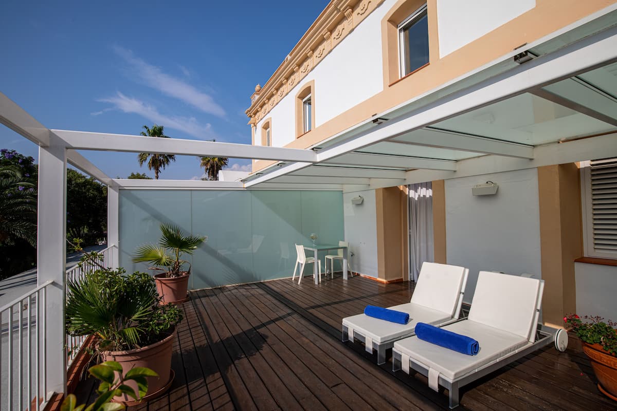 Un espacio exterior cubierto con piso de madera, sillones blancos de lounge y plantas en macetas.