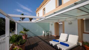 Un espacio exterior cubierto con piso de madera, sillones blancos de lounge y plantas en macetas.