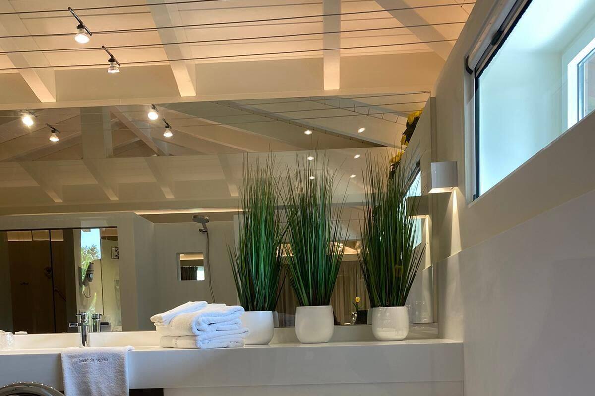 Un baño moderno con una bañera grande, un lavamanos y un espejo. Hay plantas en macetas en el alféizar de la ventana y toallas ordenadas.