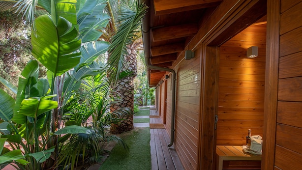 A wooden cabin with a small porch, a stone wall, and lush greenery.