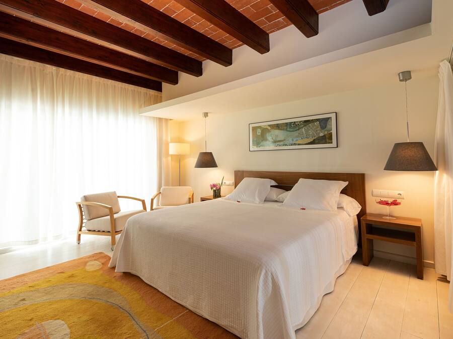 Habitación de hotel con una cama grande, dos mesitas de noche, una silla y un cuadro en la pared.