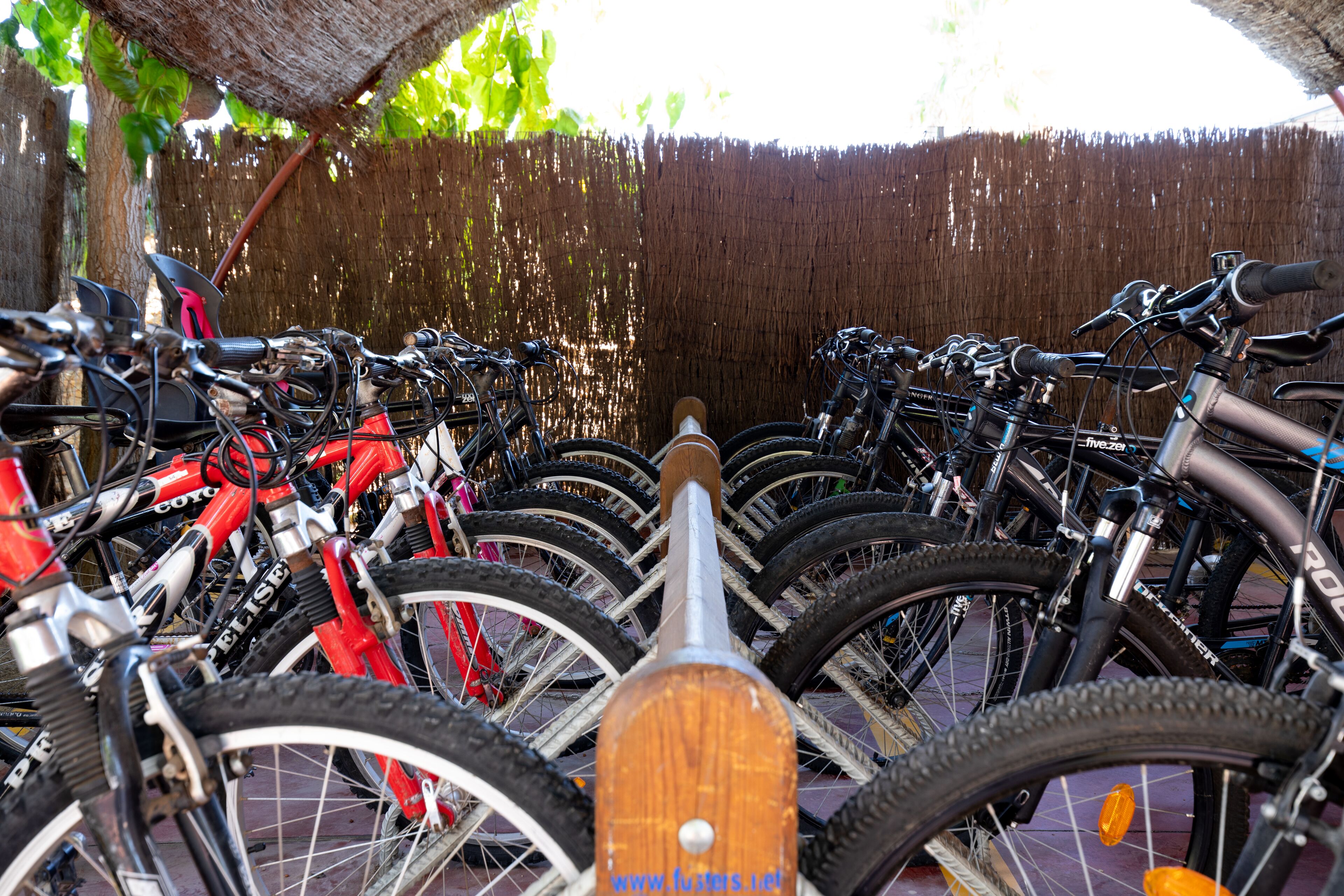 A row of bicycles parked in an outdoor area with a wooden fence in the background.
