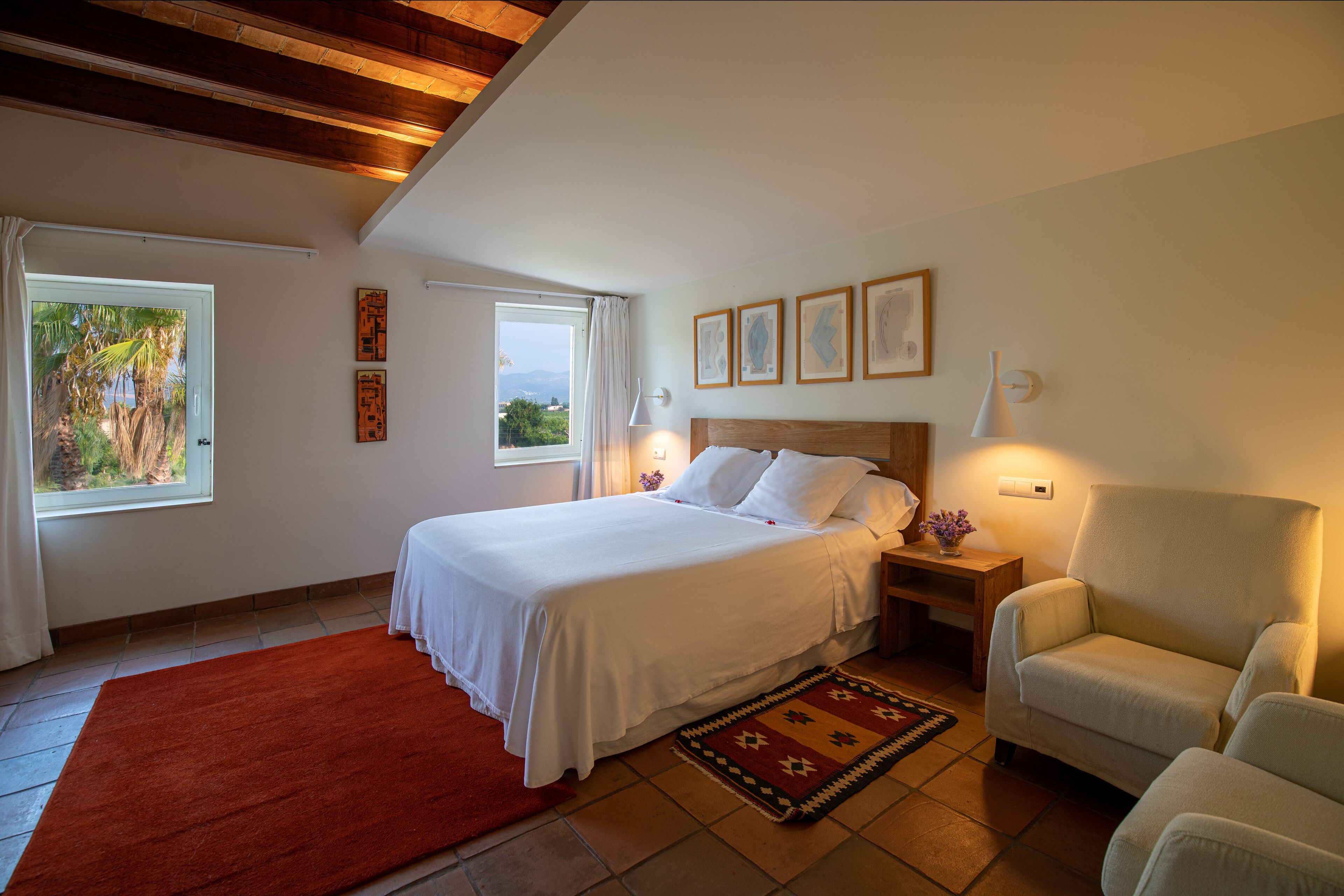 A bedroom with a bed, a chair, a nightstand, and a window with a view of greenery.