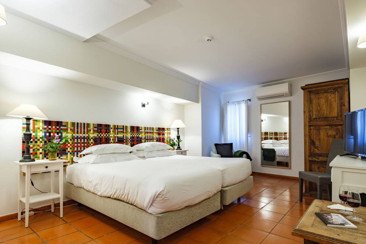 Una habitación de hotel con una cama grande, un escritorio, una silla, un televisor y una obra de arte de colores en la pared.