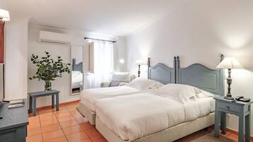 A hotel room with two beds, a small table, a lamp, a mirror, and a potted plant.