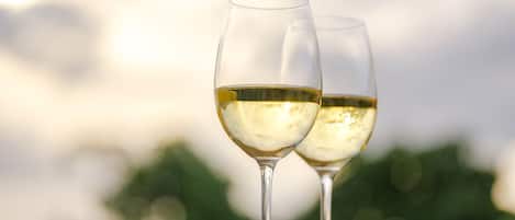Two wine glasses on a table with a blurred background of greenery and a cloudy sky.