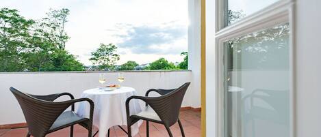 Un balcon avec une table et des chaises, une nappe blanche et deux verres de vin blanc.