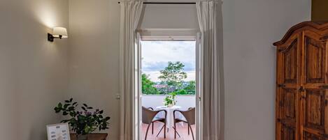 A room with a wooden cabinet, a bench with a framed photo, a potted plant, and a view through a doorway to an outdoor seating area.