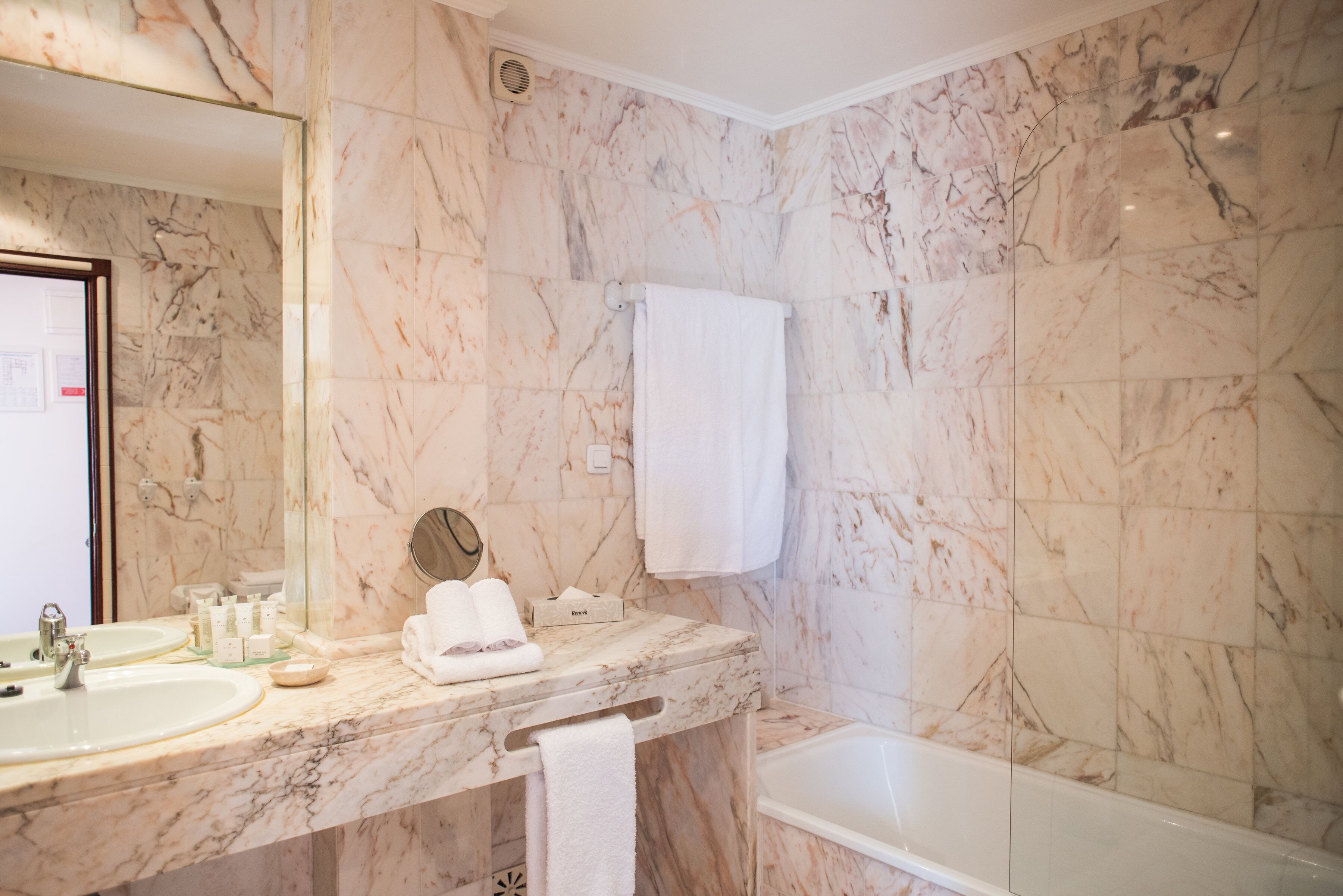 A bathroom with marble walls, a bathtub, a sink, and a mirror.