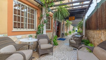 A covered outdoor seating area with wicker furniture, a small table, and potted plants.