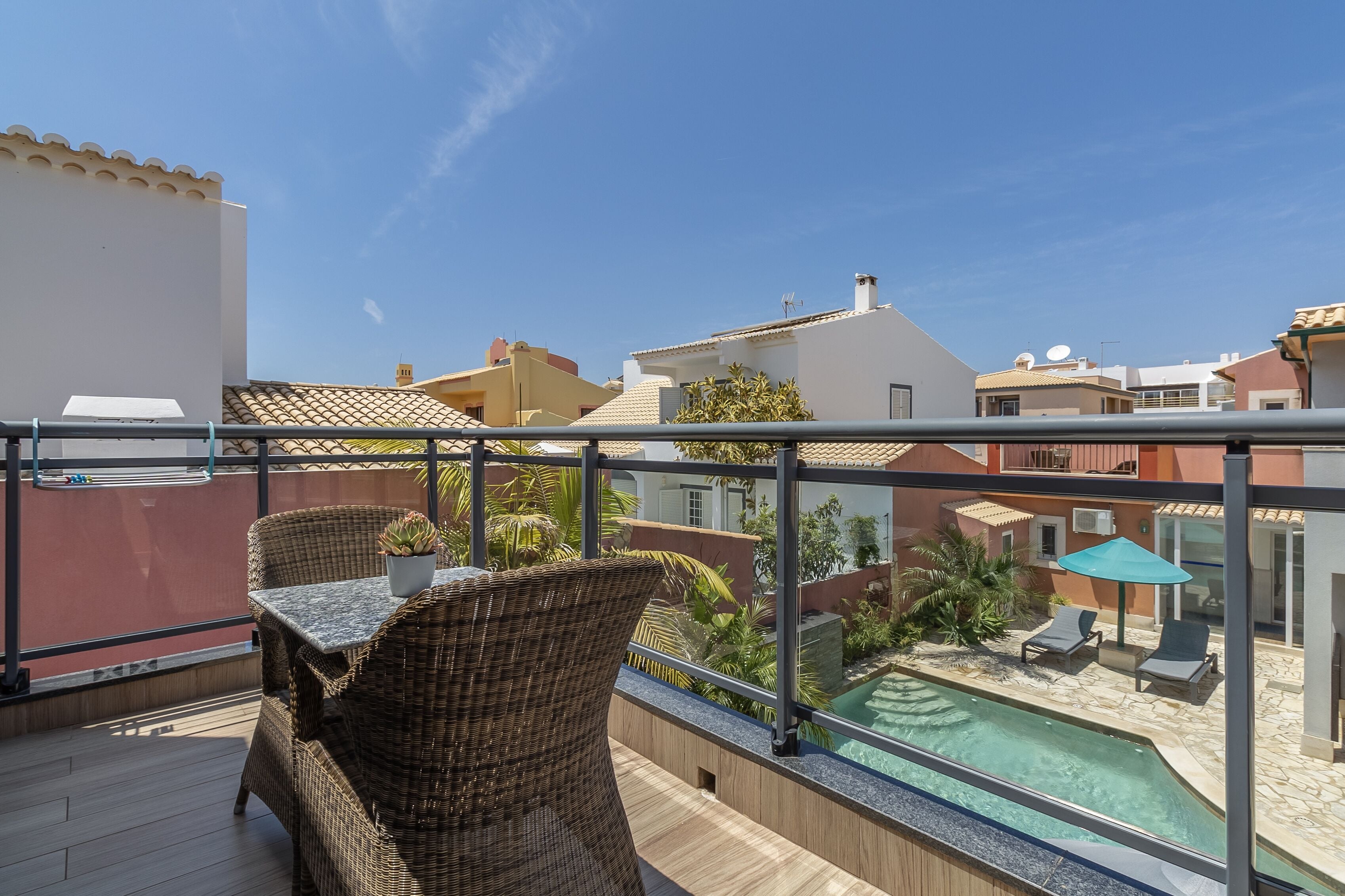 Varanda com móveis de vime, piscina e vista para edifícios próximos.