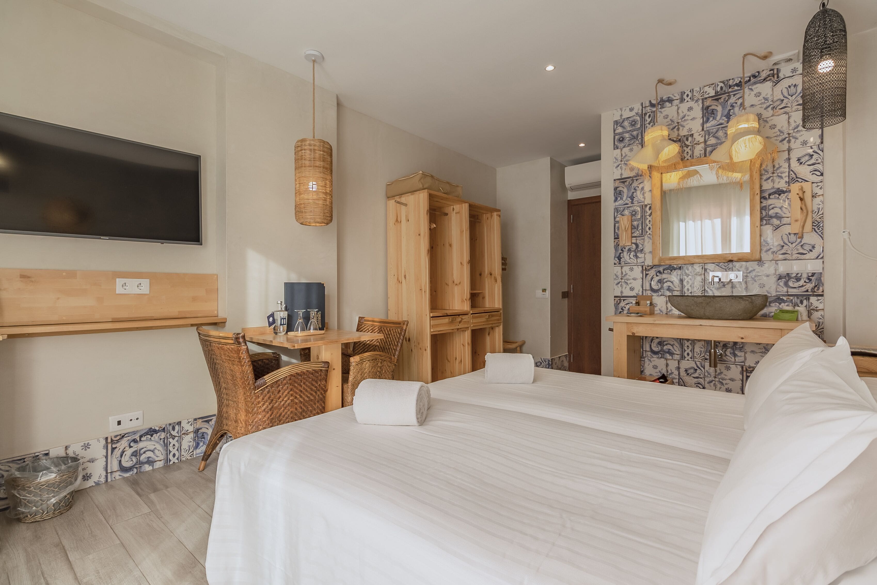 Ein Hotelzimmer mit einem großen Bett, einem Fernseher, einem Holzschrank, einem kleinen Tisch mit Stühlen sowie einem Badezimmer mit Spiegel und Waschbecken.