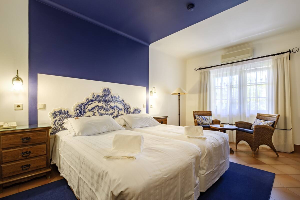 A hotel room with a large bed, two bedside tables, a desk with a chair, a dresser, and a window with curtains.