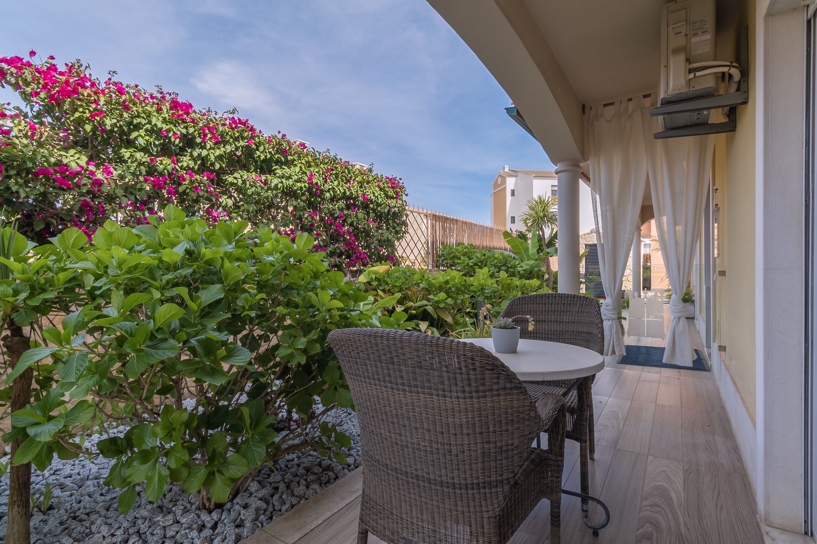 An outdoor patio with wicker furniture, a potted plant, and a view of a building in the background.