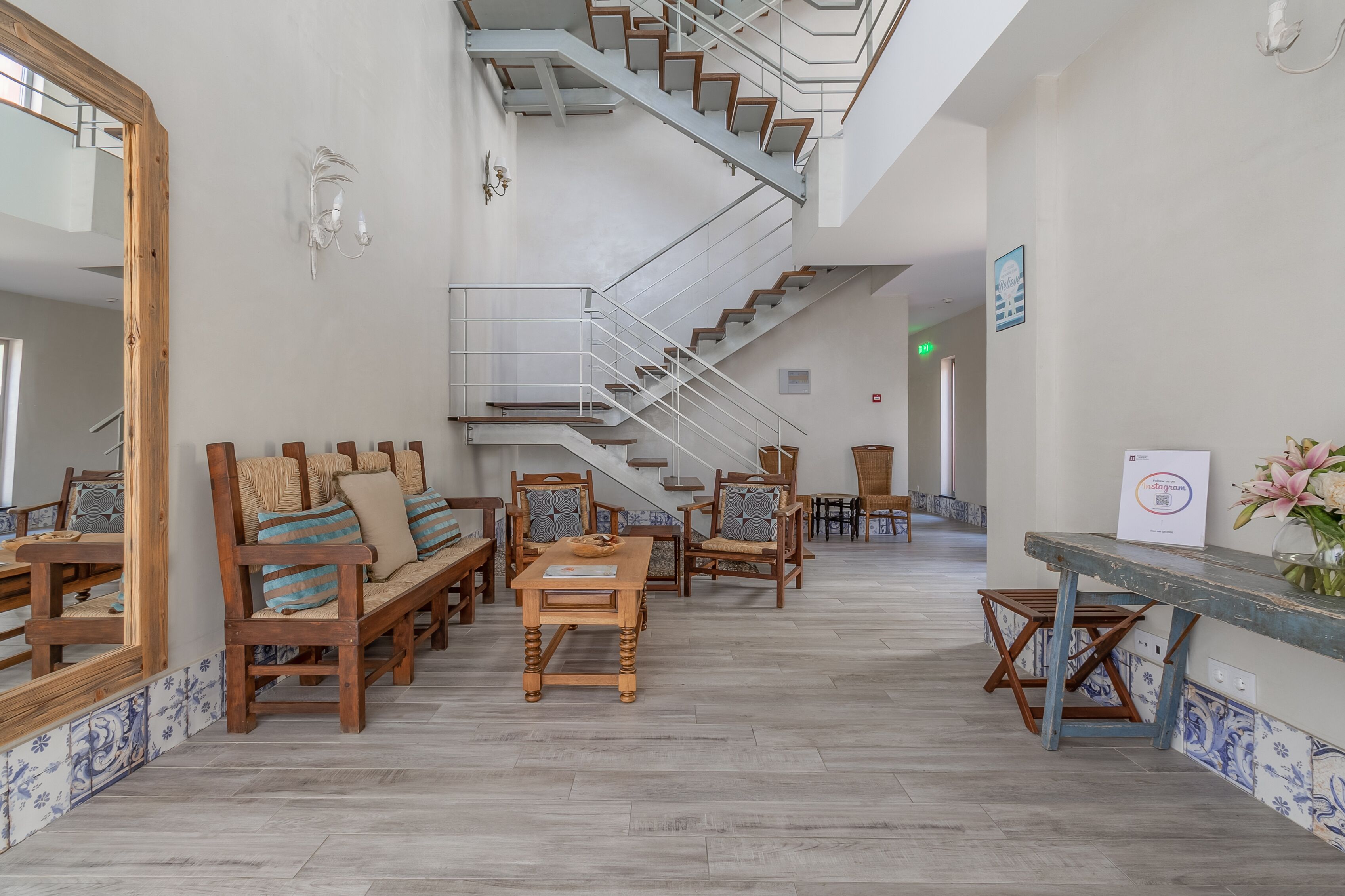 A spacious lobby with a central staircase, wooden furniture, and a tiled floor.