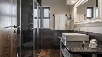 Un baño moderno con ducha envuelta en vidrio, un lavamanos blanco y un espejo grande.