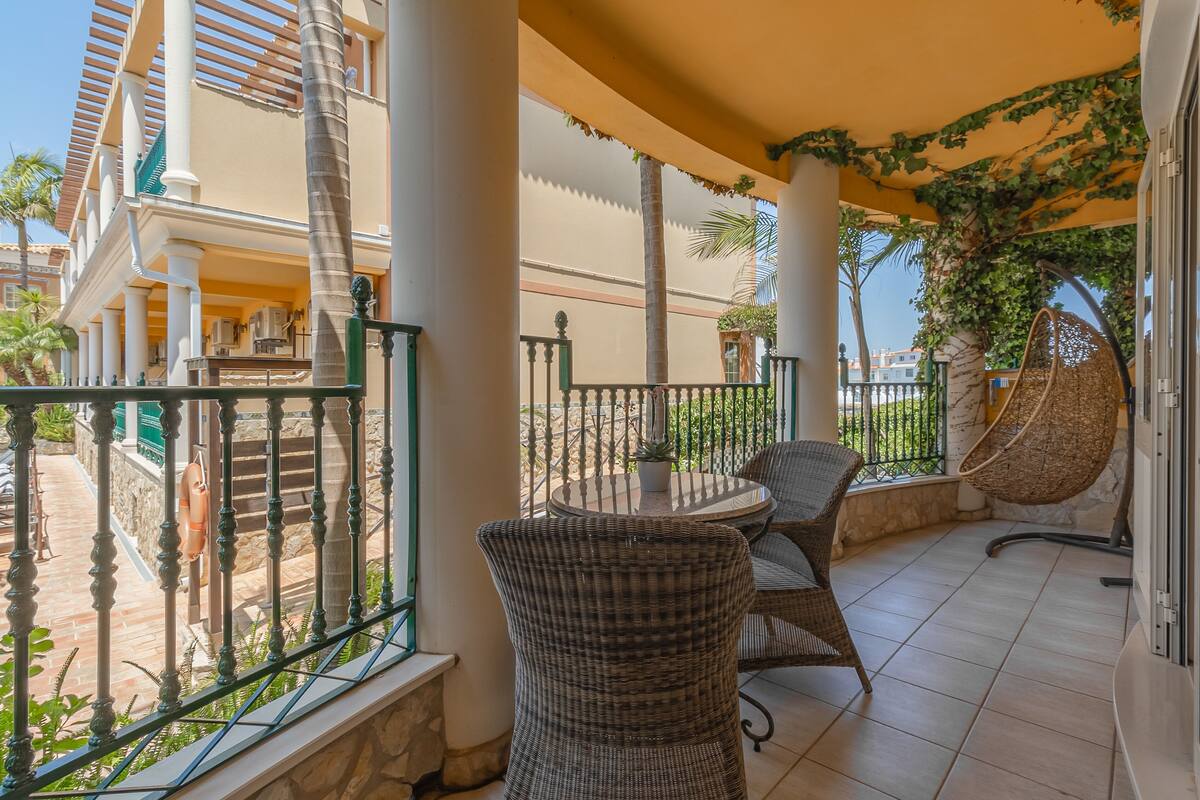 A balcony with wicker furniture, a hanging chair, and a view of the surrounding buildings.