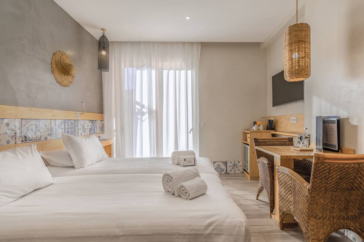 A hotel room with a large bed, a desk, a television, and a wicker chair.