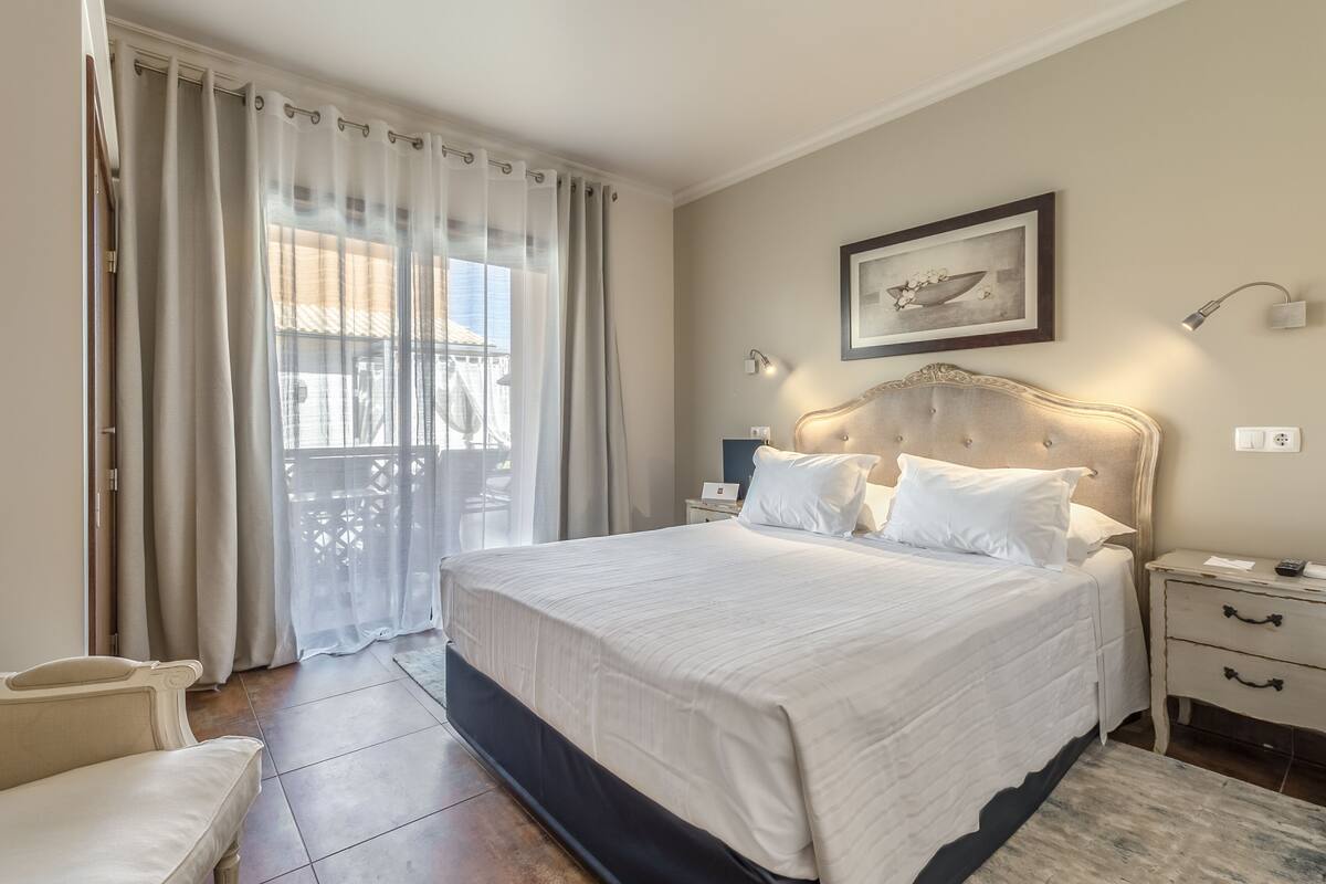 A bedroom with a large bed, a nightstand, a lamp, and a window with curtains.