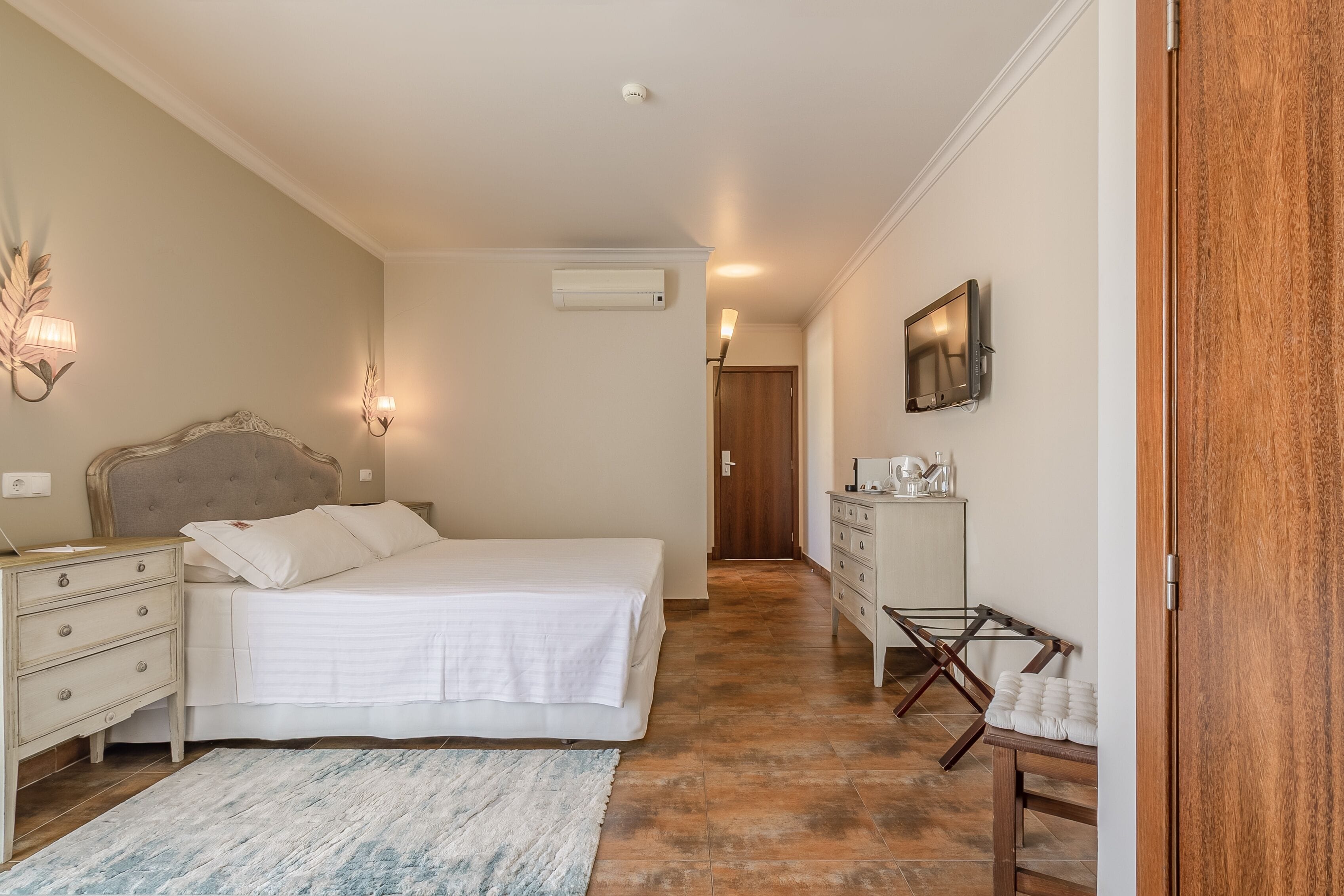 Een slaapkamer met een bed, een dressoir, een nachtkastje en een aan de muur bevestigde televisie.