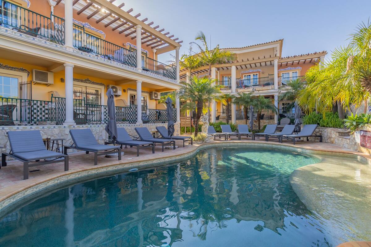 A pool area with lounge chairs and a building with balconies.