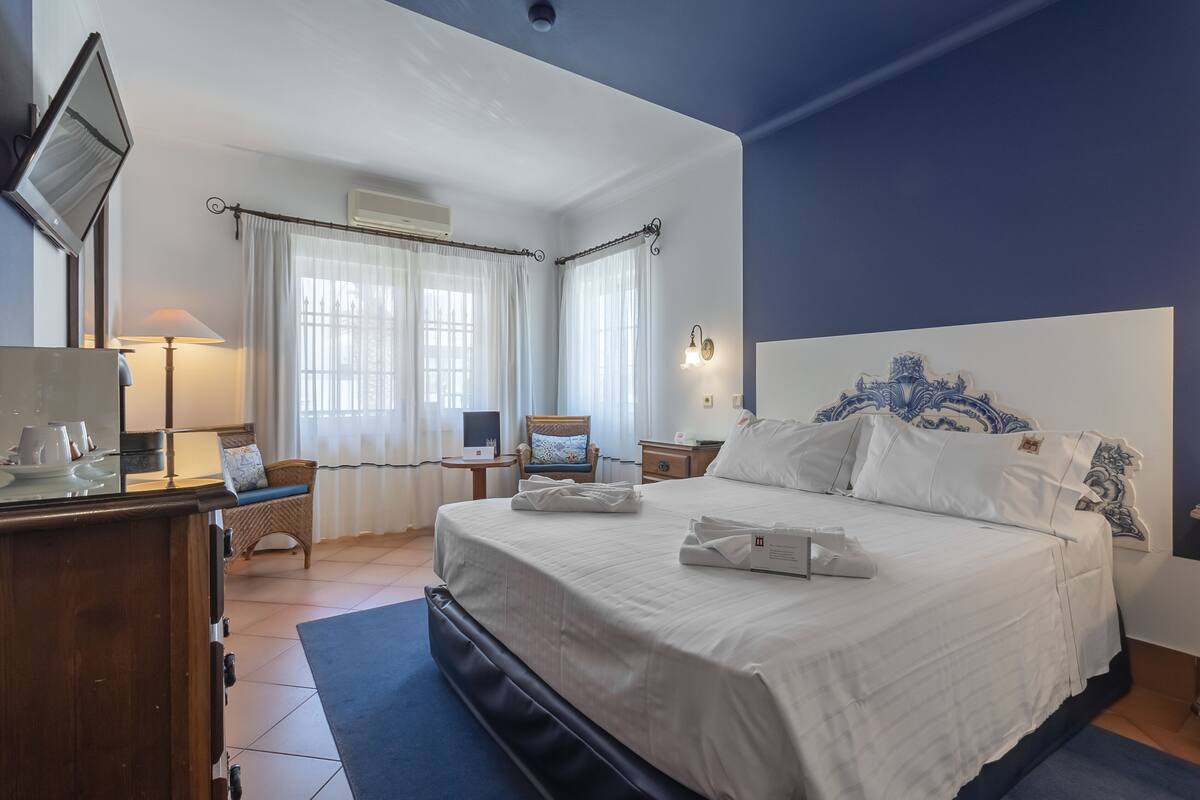 A hotel room with a large bed, a desk with a lamp, a chair, and a television.