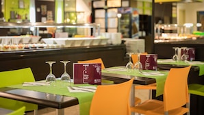 Un restaurante con mesas dispuestas para comer, con manteles verdes y sillas naranjas.