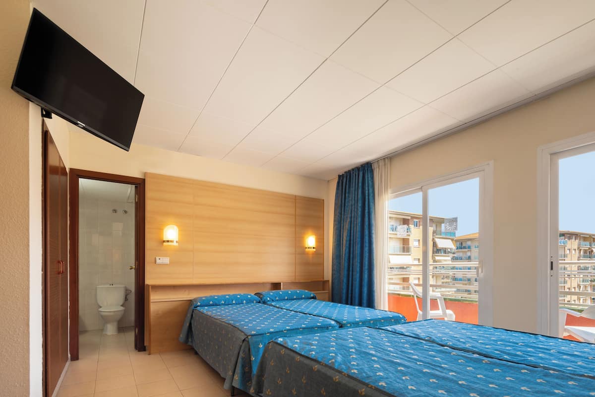 A hotel room with a bed, a TV, a bathroom, and a balcony with a view of buildings.