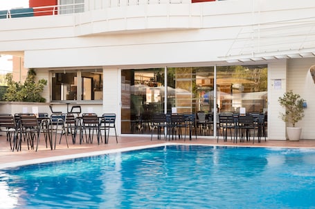 A pool area with chairs and tables, a building with large windows, and a sign indicating a restaurant.