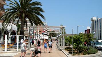 A pedestrian walkway lined with palm trees and a covered area with seating.