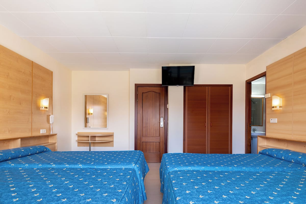 A hotel room with two beds, a wooden wardrobe, a TV mounted on the wall, and a bathroom visible through an open door.