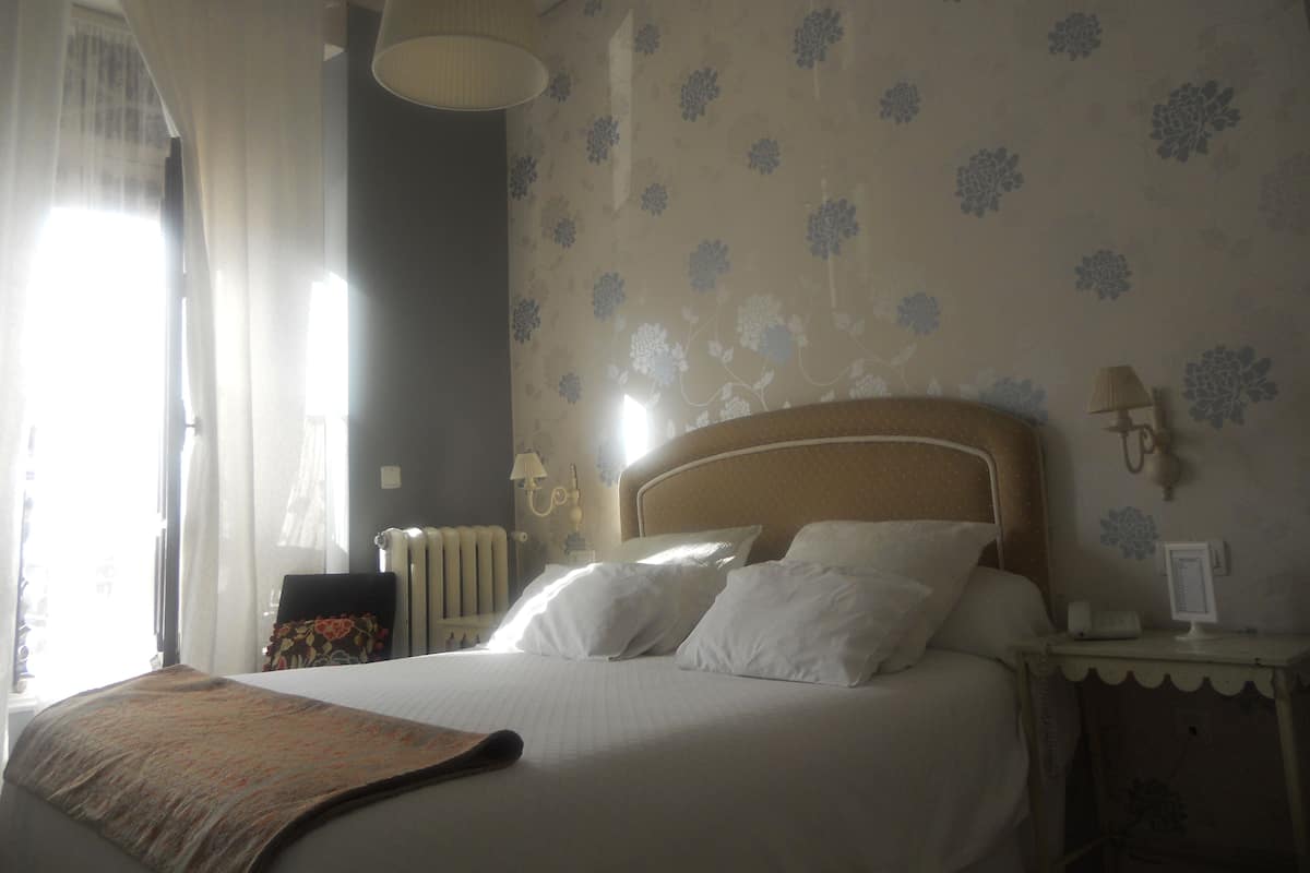 A hotel room with a bed, a nightstand, a lamp, and a window with curtains.