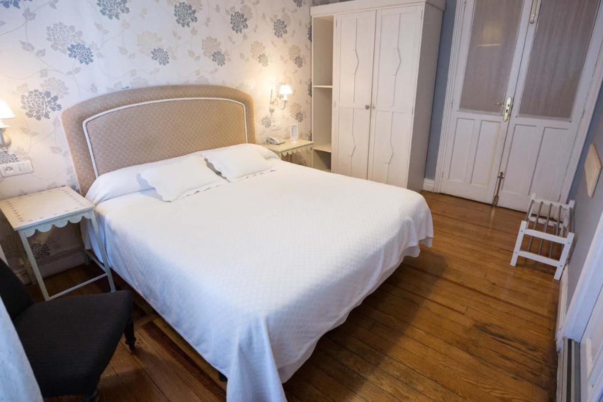 A bedroom with a bed, bedside table, lamp, wardrobe, and a chair.