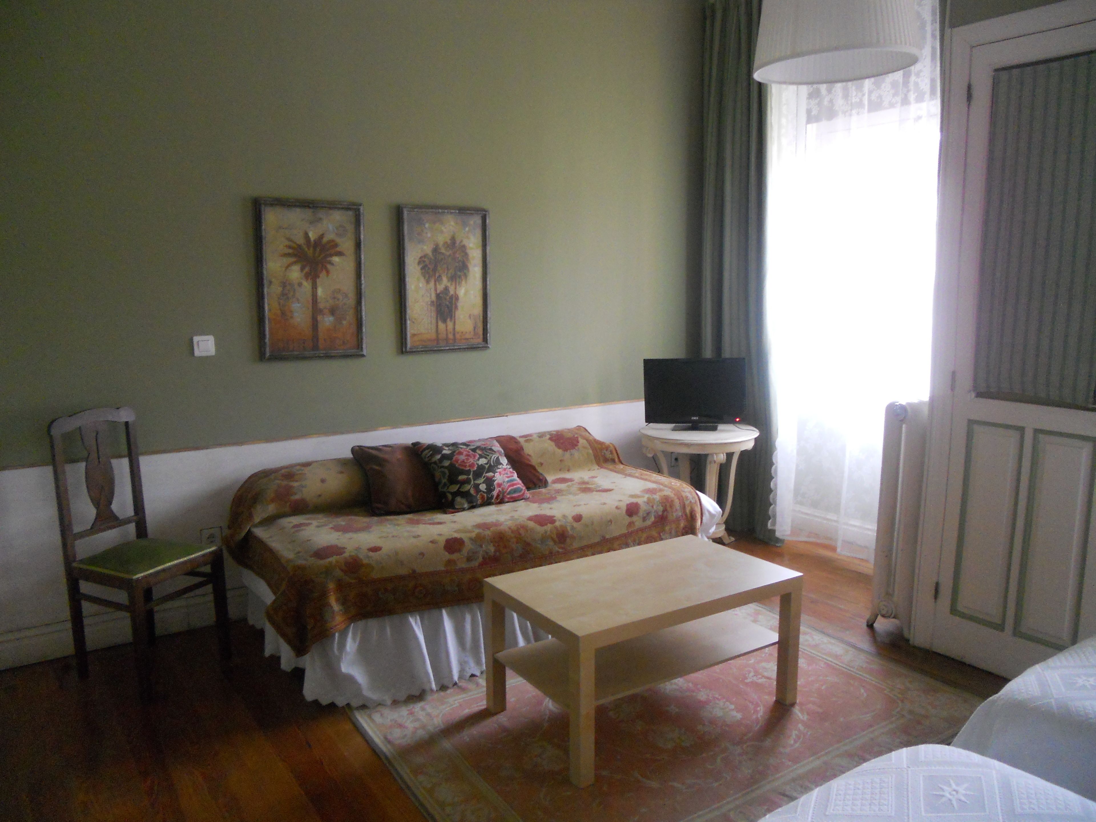A room with a bed, a chair, a small table, and a television on a side table.