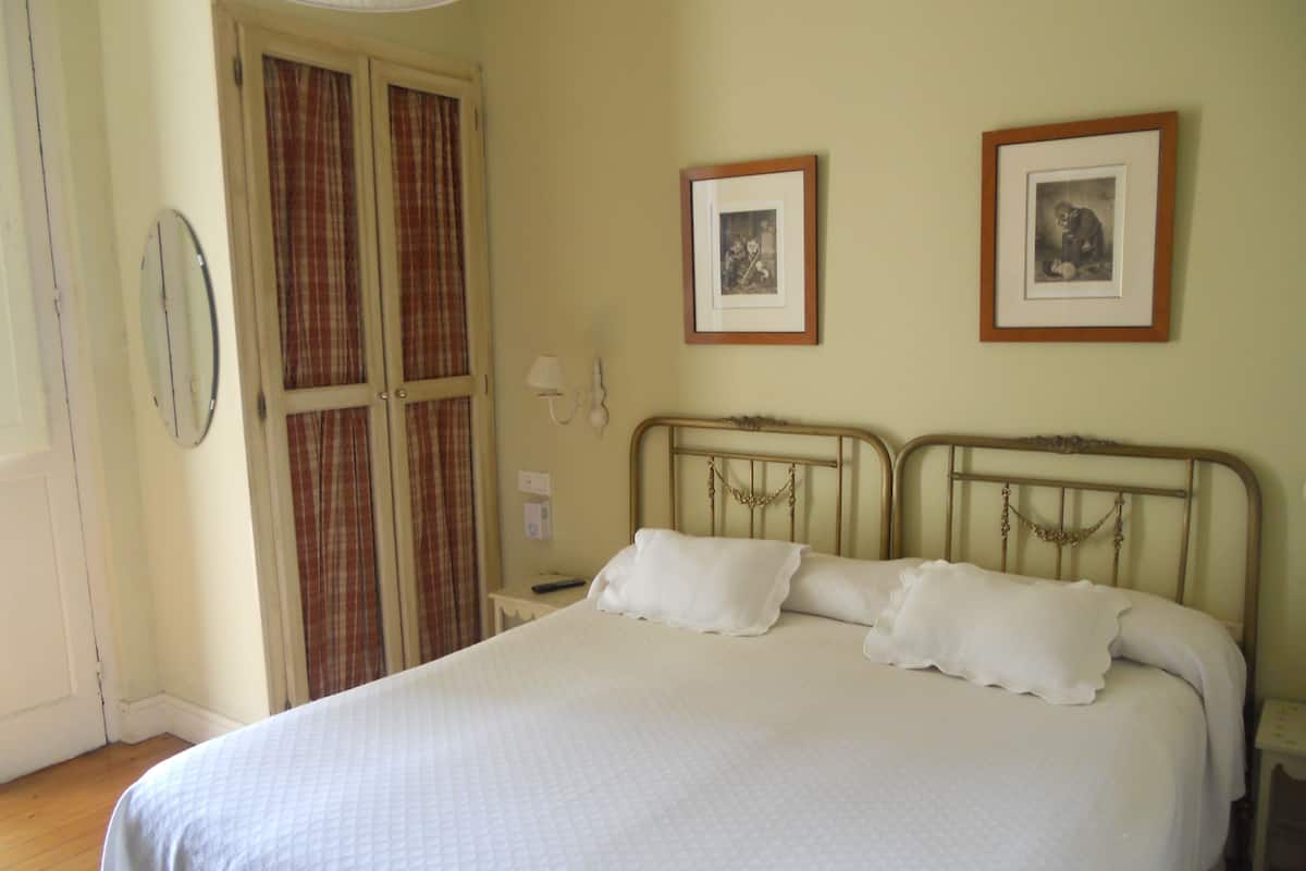 A bedroom with a bed, a nightstand, a wall-mounted lamp, and two framed pictures.