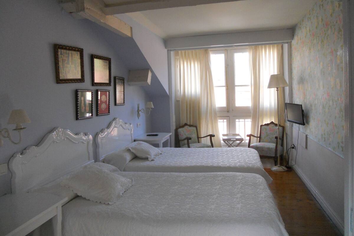 A hotel room with two beds, a small table, chairs, a TV, and a window with curtains.