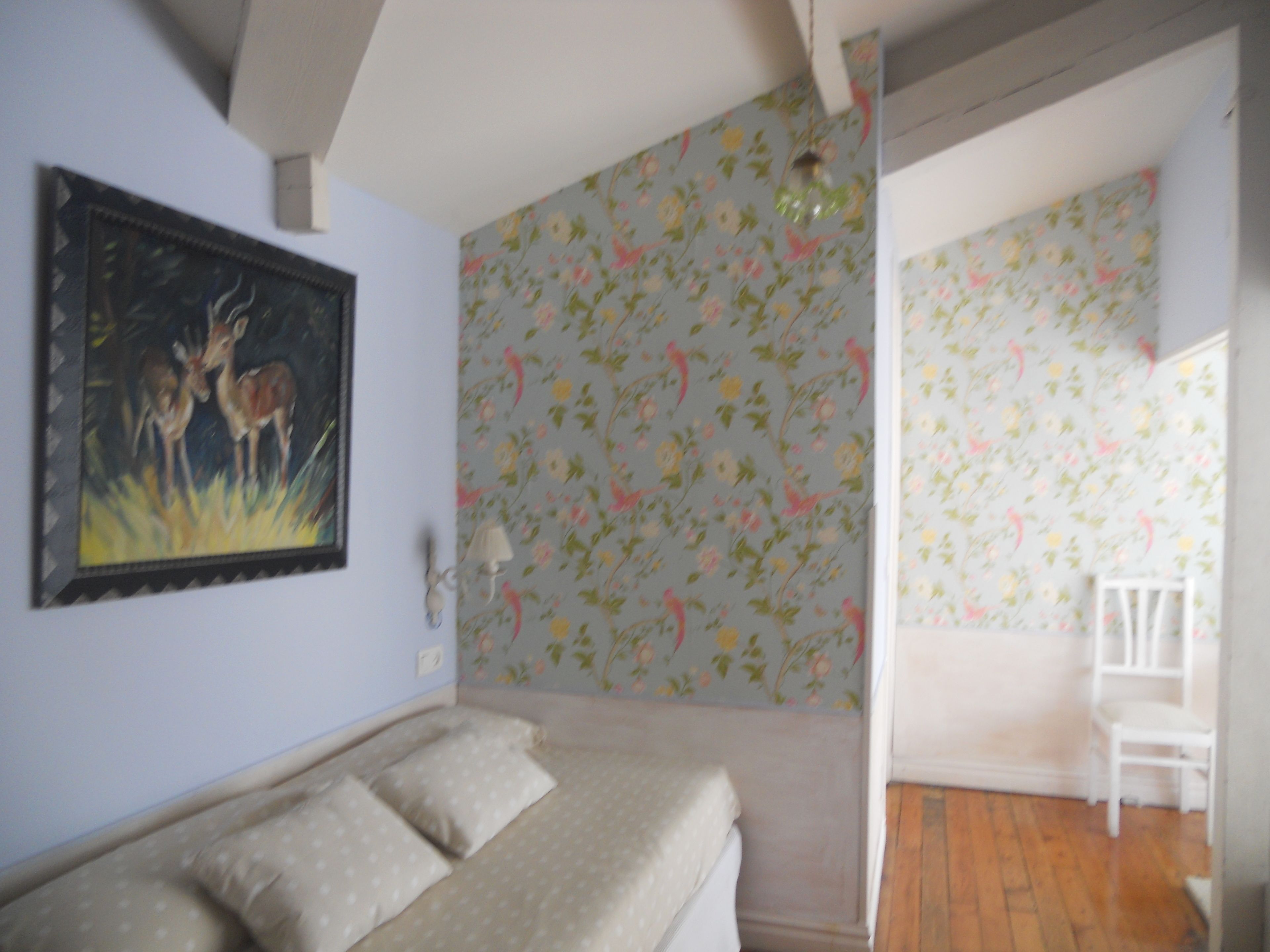 Quarto com uma cama, um quadro de veados, papel de parede floral e uma cadeira branca.