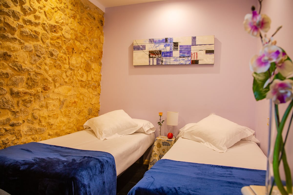 A room with two beds, a stone wall, a painting, and a flower.