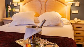 A hotel room with a bed, two bedside lamps, a nightstand with a phone, and a tray with a rose and a glass.