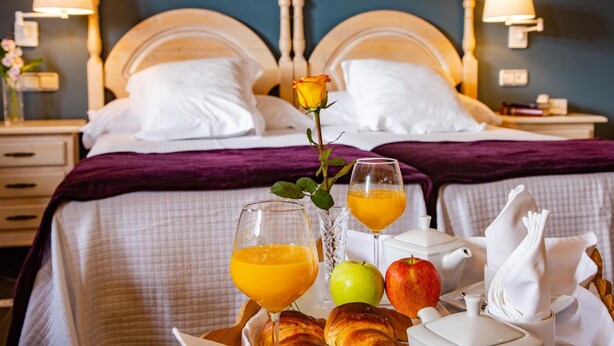 Quarto de hotel com duas camas, bandeja de café da manhã com croissants, maçãs, suco e uma rosa.