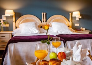A hotel room with two beds, a breakfast tray with croissants, apples, juice, and a rose.