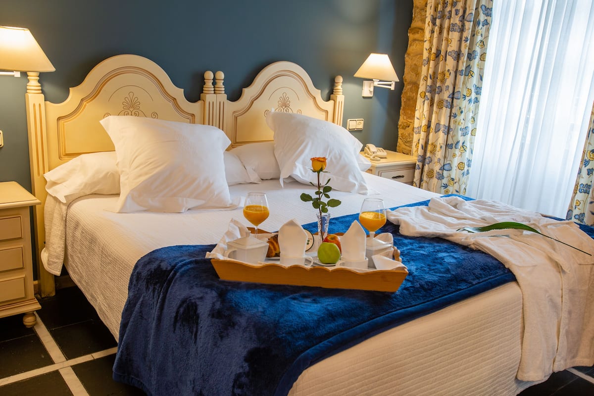 A hotel room with a large bed, white bedding, a blue blanket, and a tray with breakfast items.